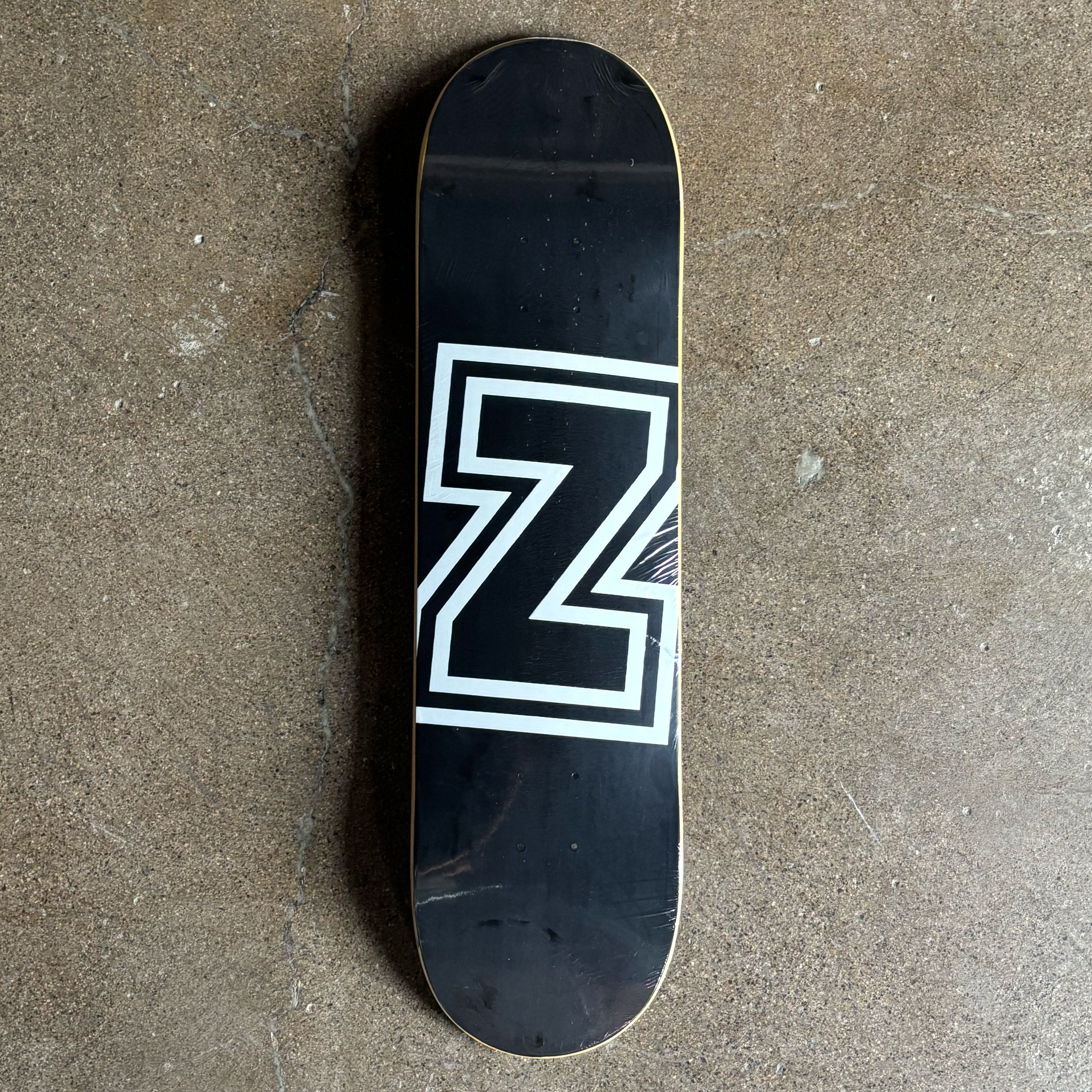 Black skateboard deck with a white logo on a concrete surface